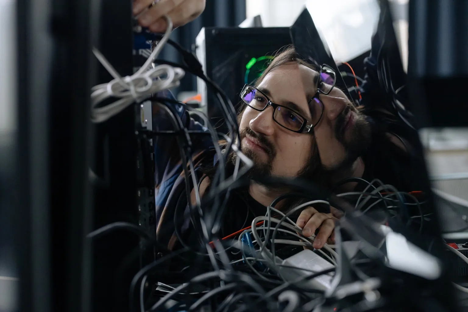 Technician reaching into a tangle of cables behind network equipment on site