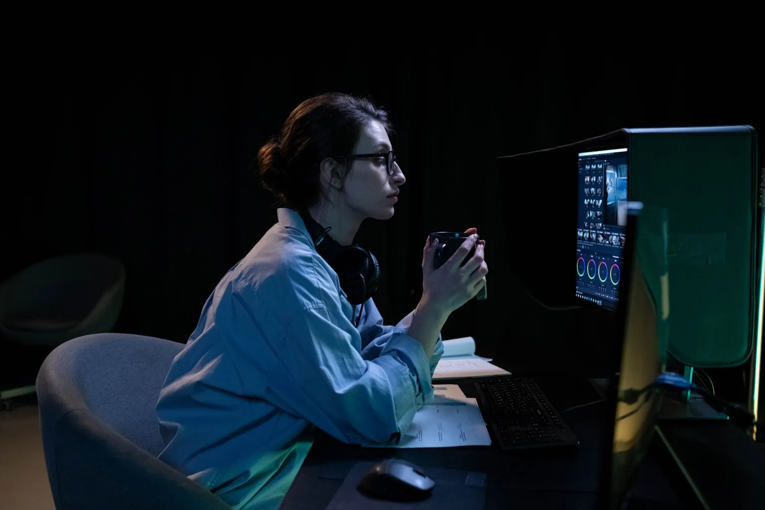 Engineer with a coffee mug at a dark desk at night, watching system dashboards