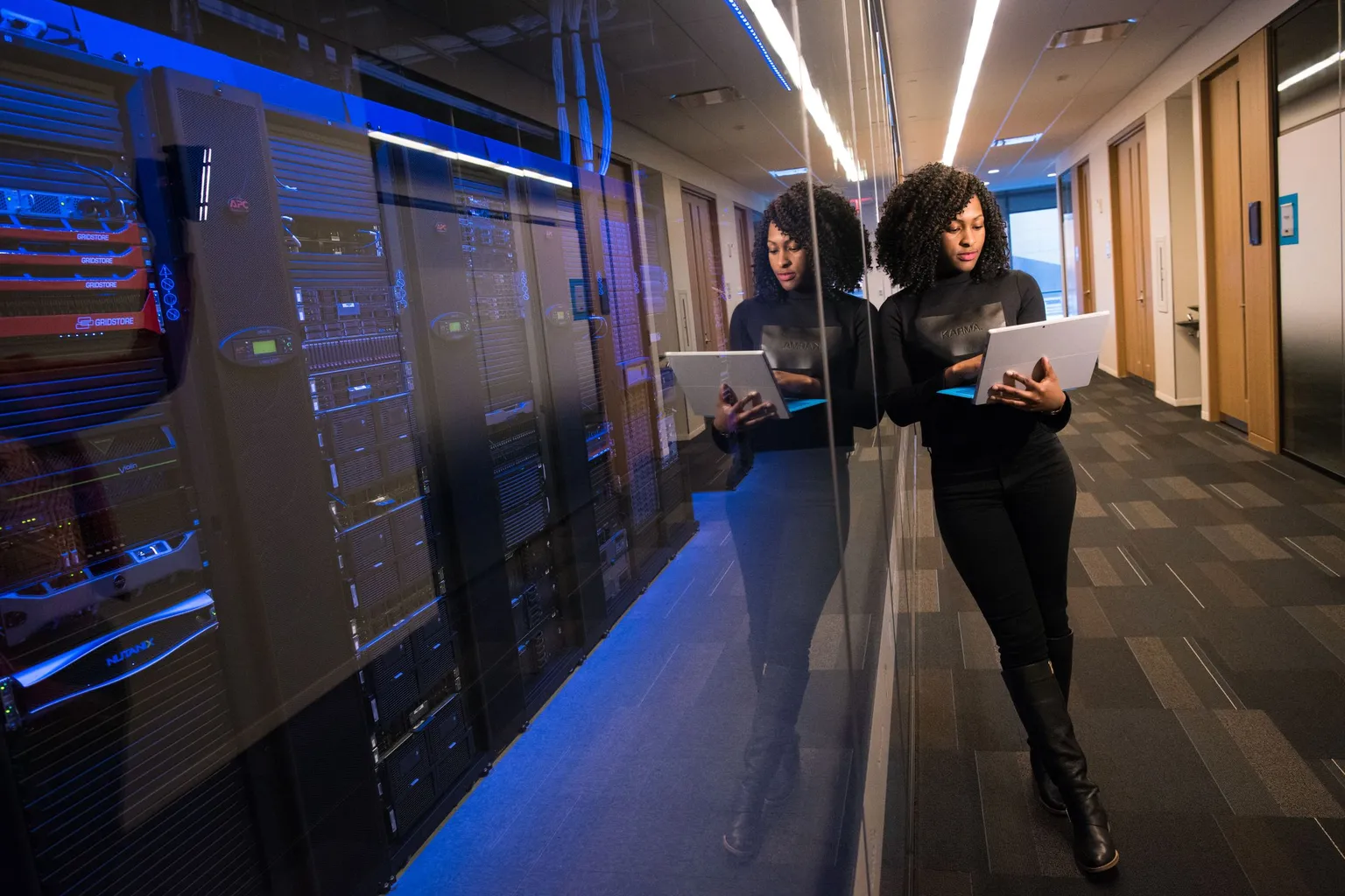 Two engineers holding laptops in a blue-lit server room aisle